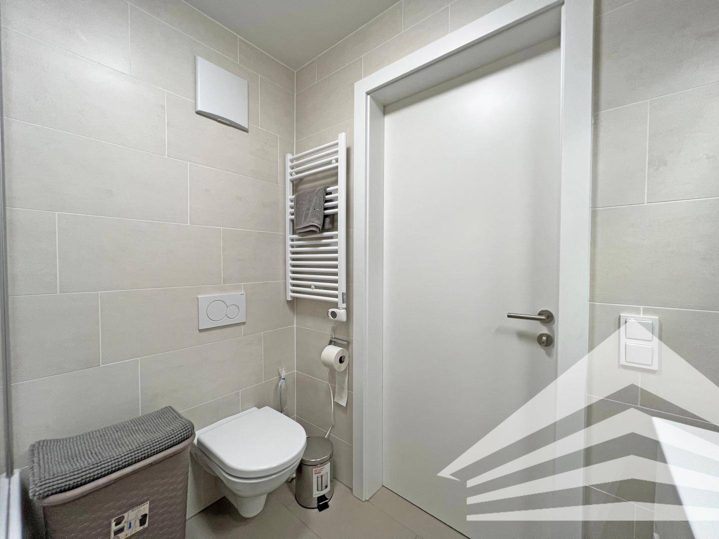 Separates WC mit Wand-WC, Handtuchheizkörper und hellen Fliesen.