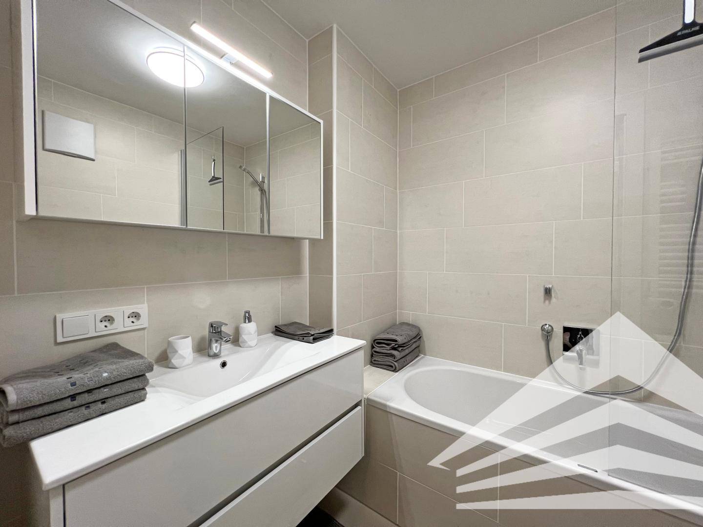 Helles Badezimmer mit Waschtisch, Spiegelschrank und Badewanne mit Duschabtrennung.