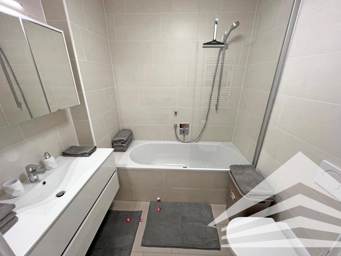 Modernes Badezimmer mit Badewanne, Duschfunktion und hellen Fliesen an Wänden und Boden.