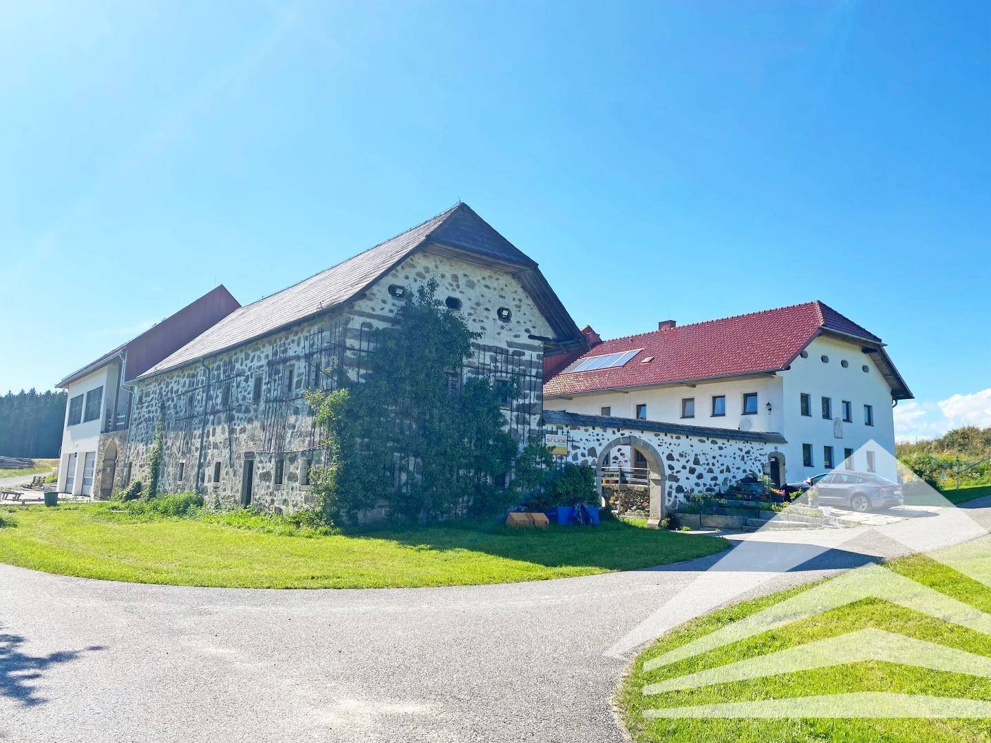 Weitläufiges Anwesen mit mehreren Gebäuden, darunter ein historisches Steinhaus und ein Neubau.