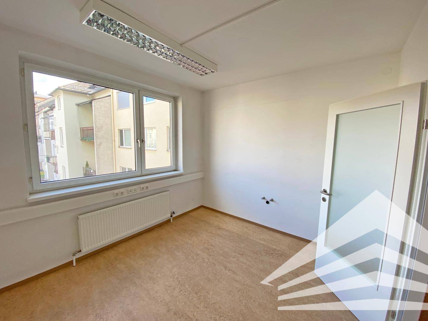 Büroraum mit Fenster und einer modernen Tür mit Milchglas, die zu einem anderen Bereich führt.