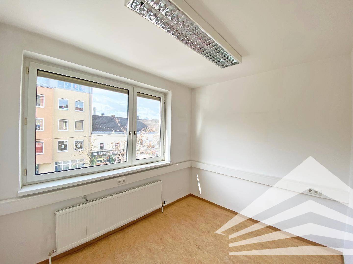 Büroraum mit großem Fenster, das viel Tageslicht hereinlässt und einen Blick auf die Straße bietet.