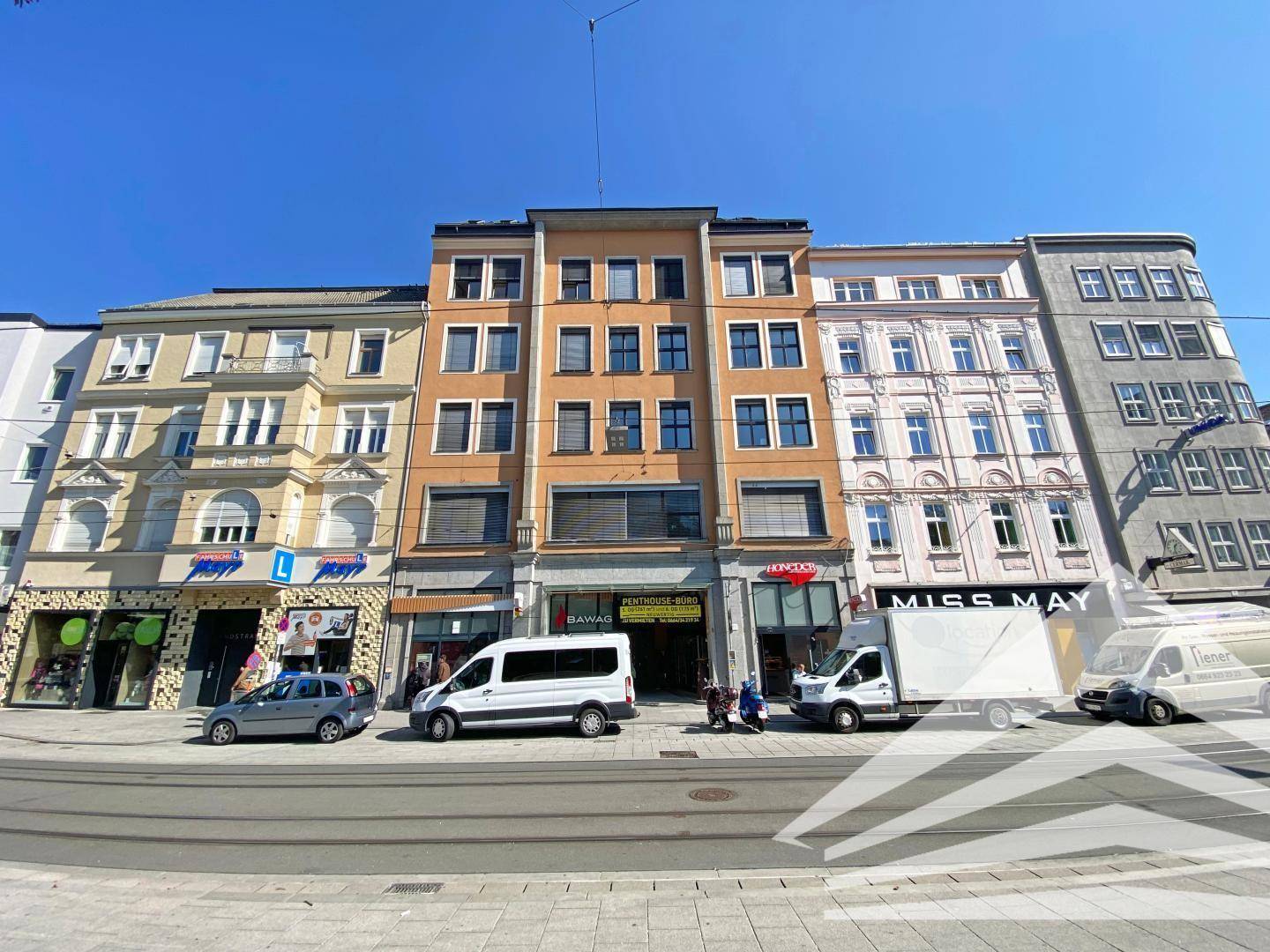 Straßenansicht eines mehrstöckigen Gebäudes mit Geschäften im Erdgeschoss und Wohnungen darüber.