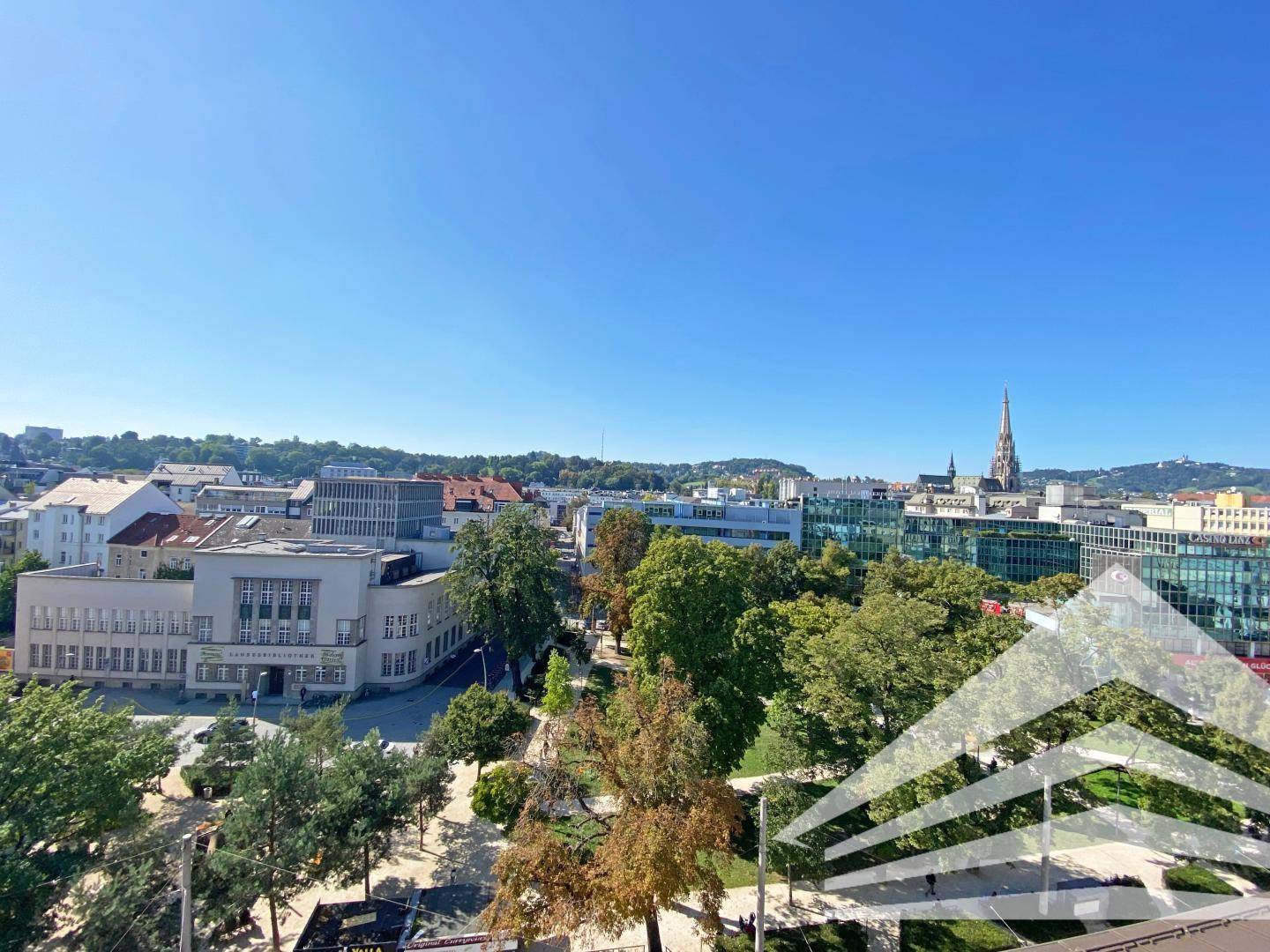 Panoramablick über die Stadt mit grünen Bäumen und historischen Gebäuden unter blauem Himmel.