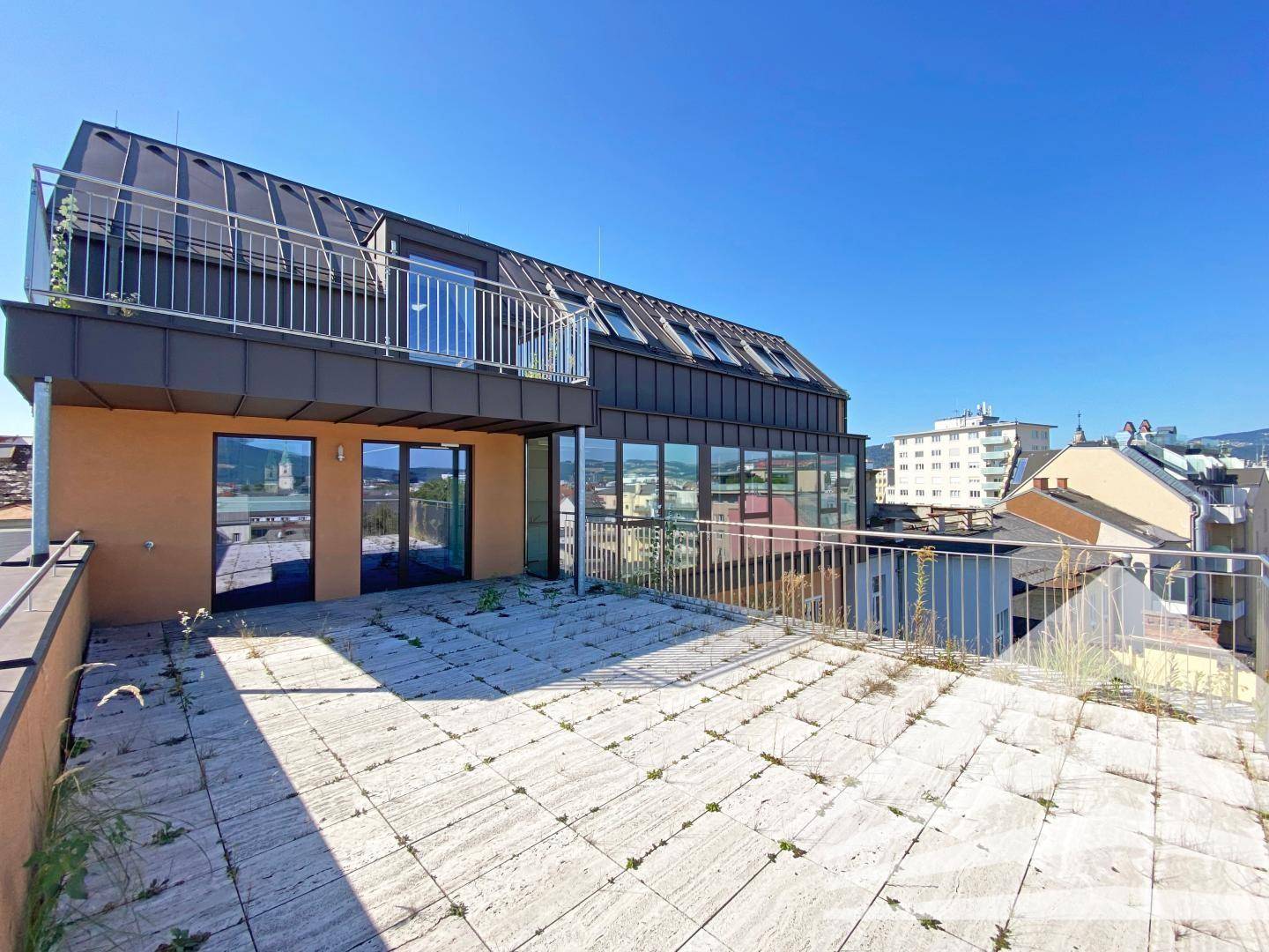 Große Dachterrasse mit Steinplatten, Metallgeländer und weitem Blick über die Stadt.
