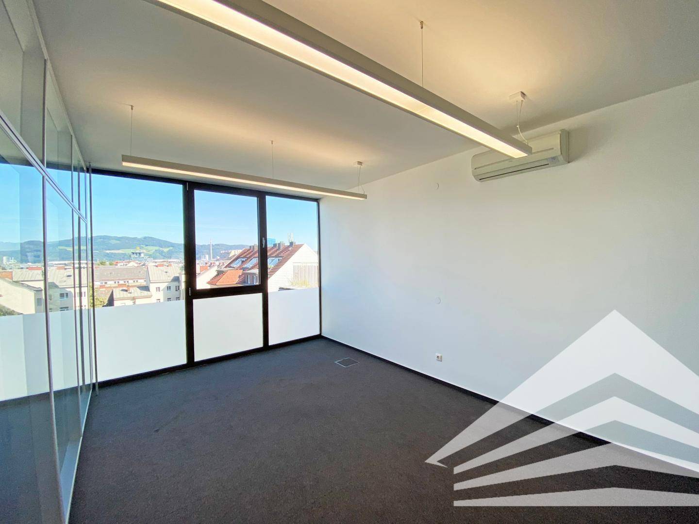 Moderner Büroraum mit Teppichboden, Klimaanlage und großen Fenstern mit Stadtblick.