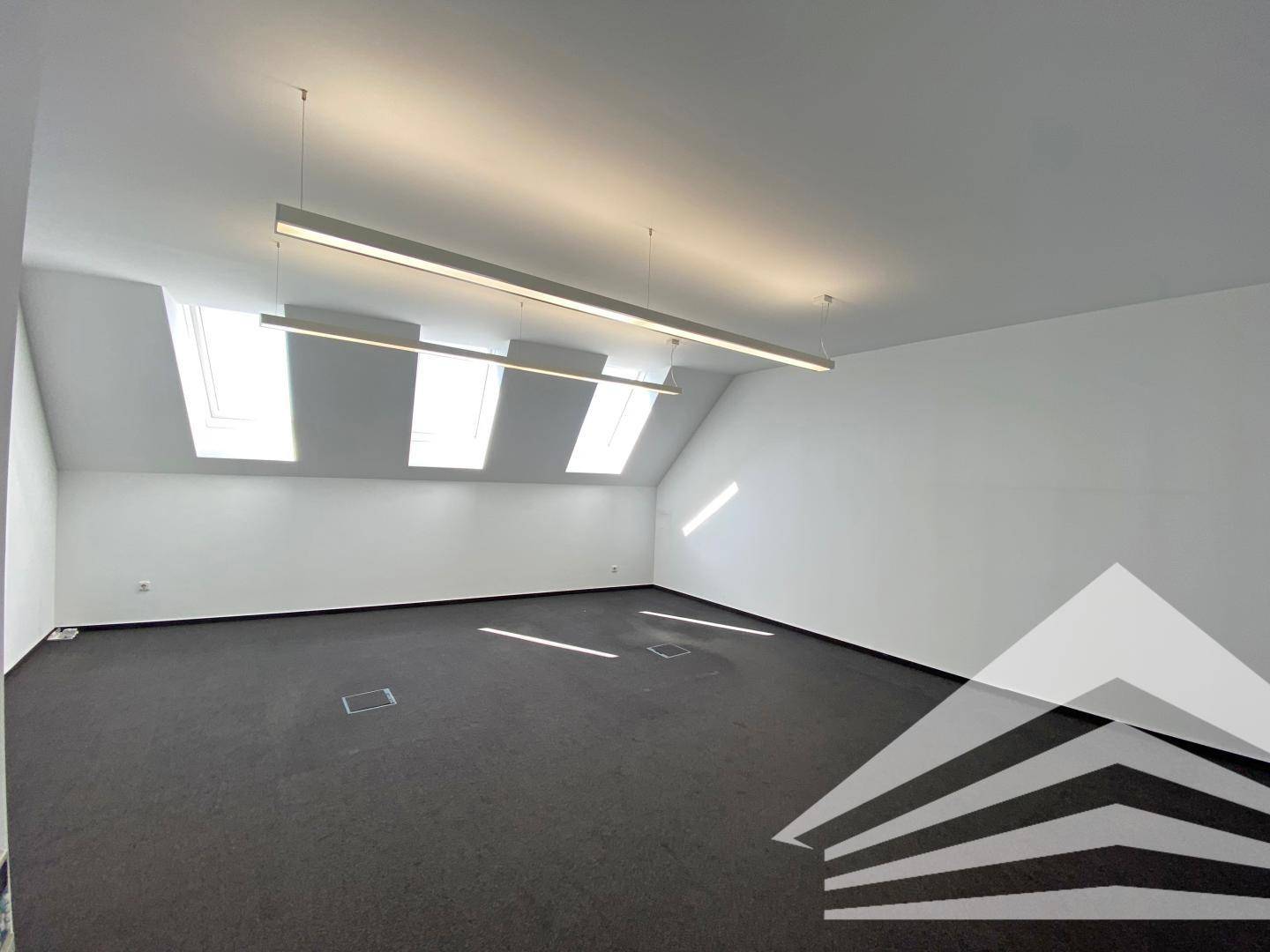 Heller Büroraum im Dachgeschoss mit Teppichboden und mehreren Dachfenstern für Tageslicht.