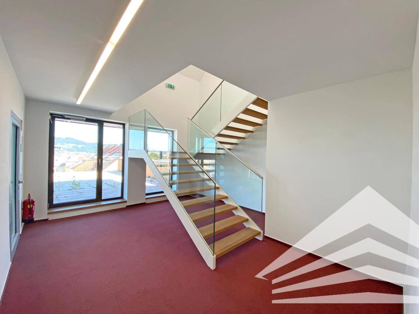 Heller Eingangsbereich mit moderner Holztreppe, Glasgeländer und Zugang zur Terrasse.