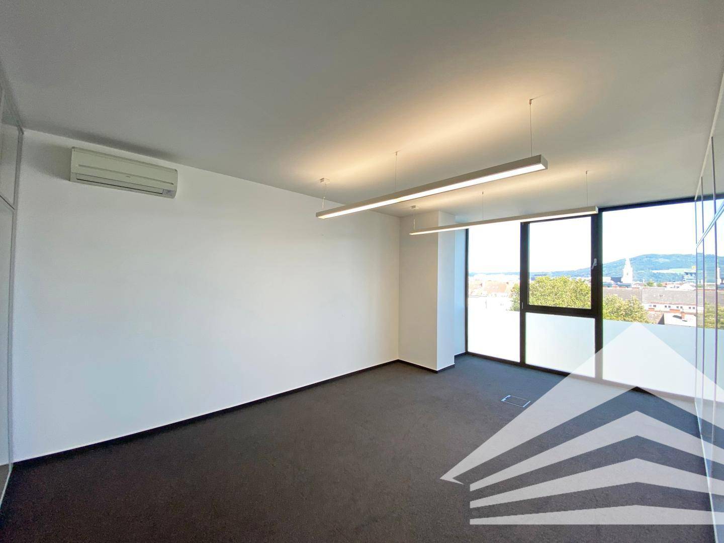 Geräumiger Büroraum mit Teppichboden, Klimaanlage und großen Fenstern mit Ausblick.
