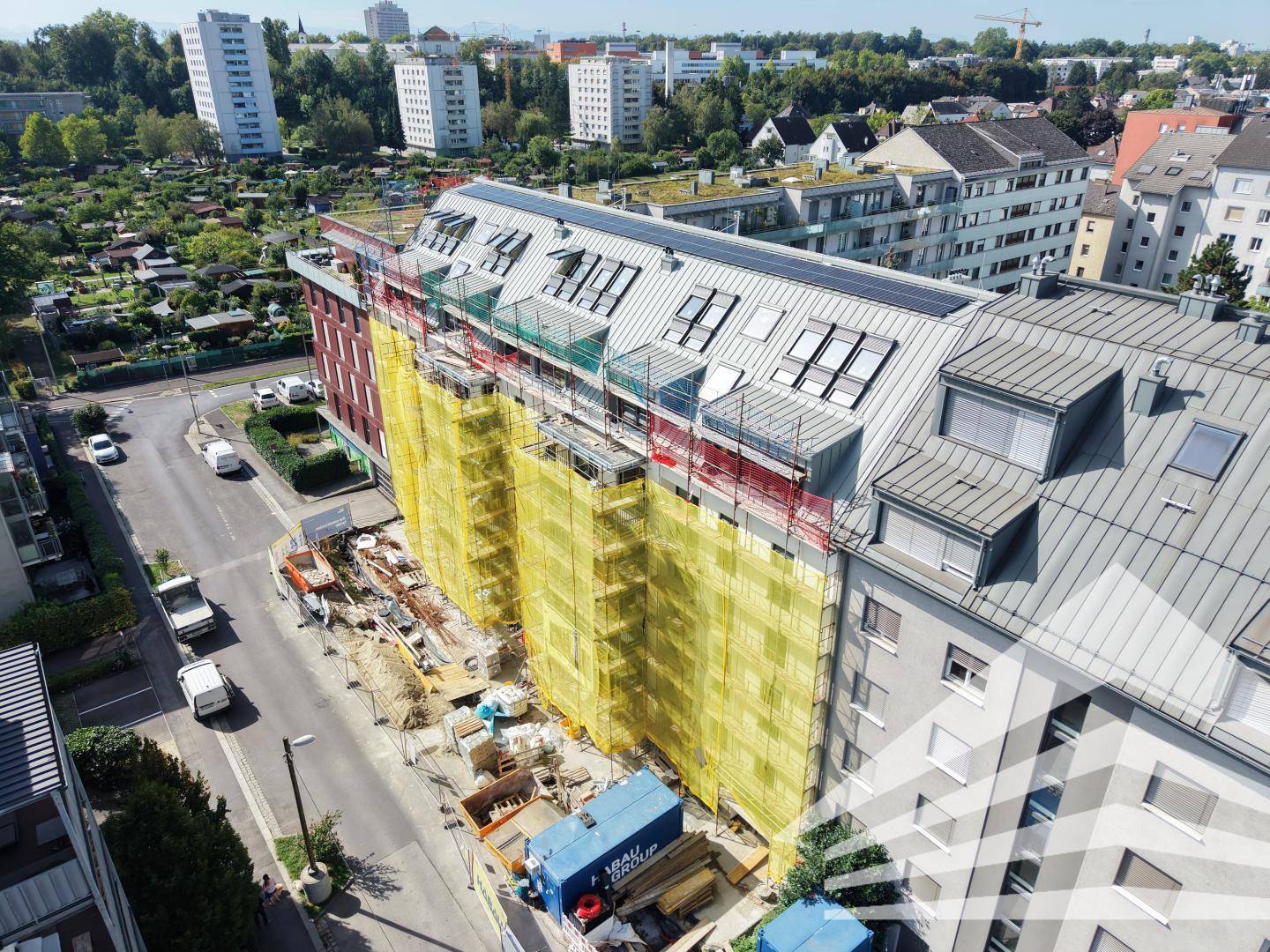 Luftaufnahme eines im Bau befindlichen Gebäudes mit Gerüst an der Seitenfassade und angrenzender Straße.