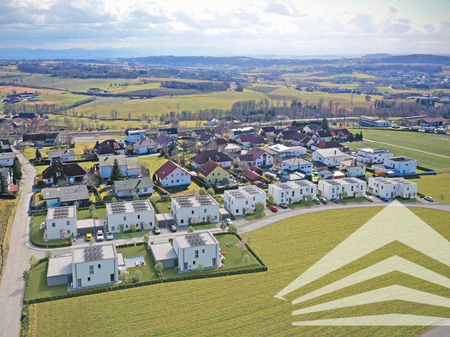 Weitläufige Luftaufnahme einer Wohngegend mit Neubauten und ländlicher Umgebung sowie Bergblick.