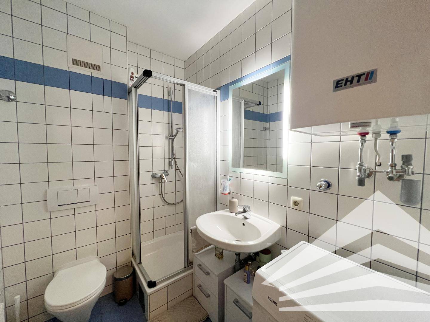 Badezimmer mit Dusche, WC, Waschbecken und Fliesen in Weiß und Blau.