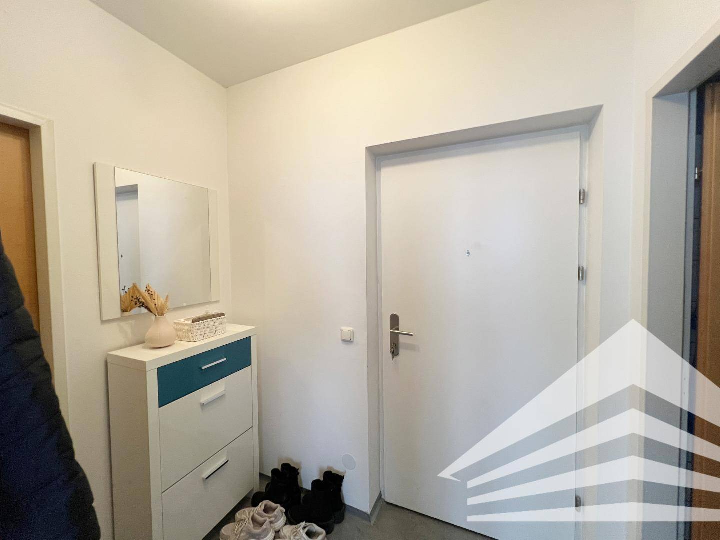 Heller Eingangsbereich mit Schuhschrank, Spiegel und weißer Wohnungstür.
