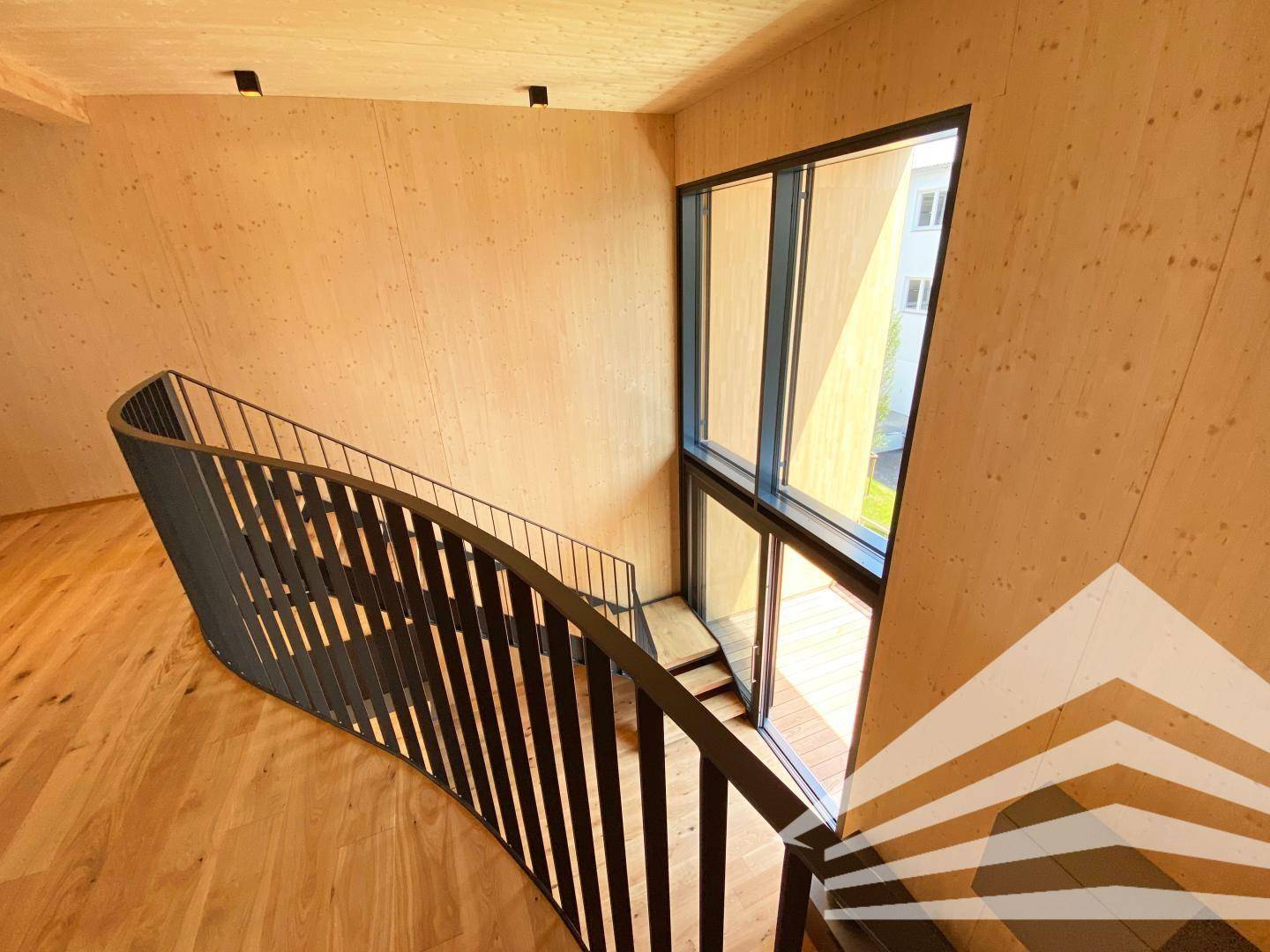 Elegante geschwungene Treppe mit schwarzem Geländer und großen Fenstern für viel Licht.