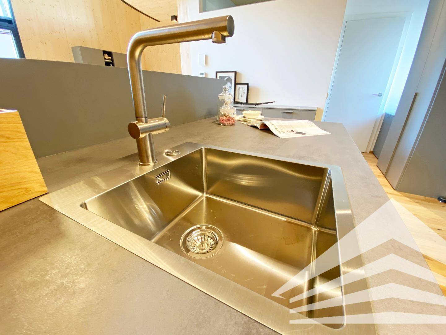 Moderne Küchenspüle mit goldfarbenem Wasserhahn und dunkler Arbeitsplatte in einem hellen Raum.