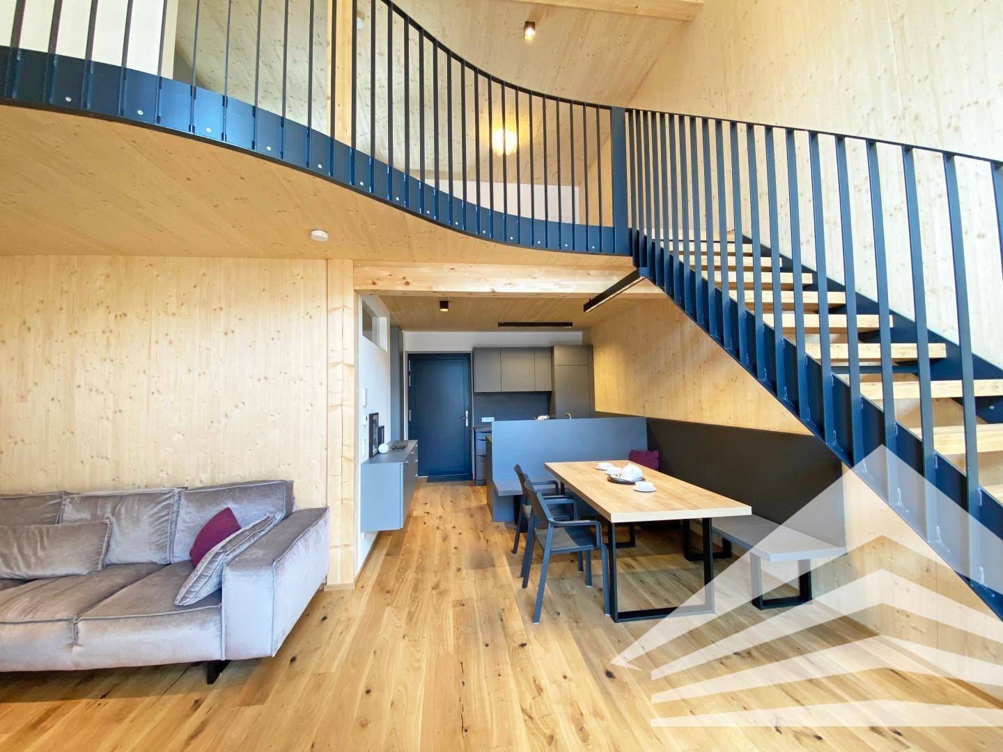 Offener Wohn- und Essbereich mit bequemer Couch, Holzboden und moderner Treppe.