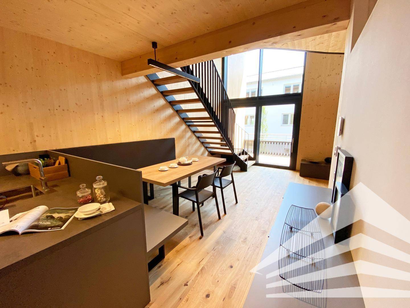 Heller Wohnbereich mit offener Treppe, Holzboden und Zugang zu einem Balkon.