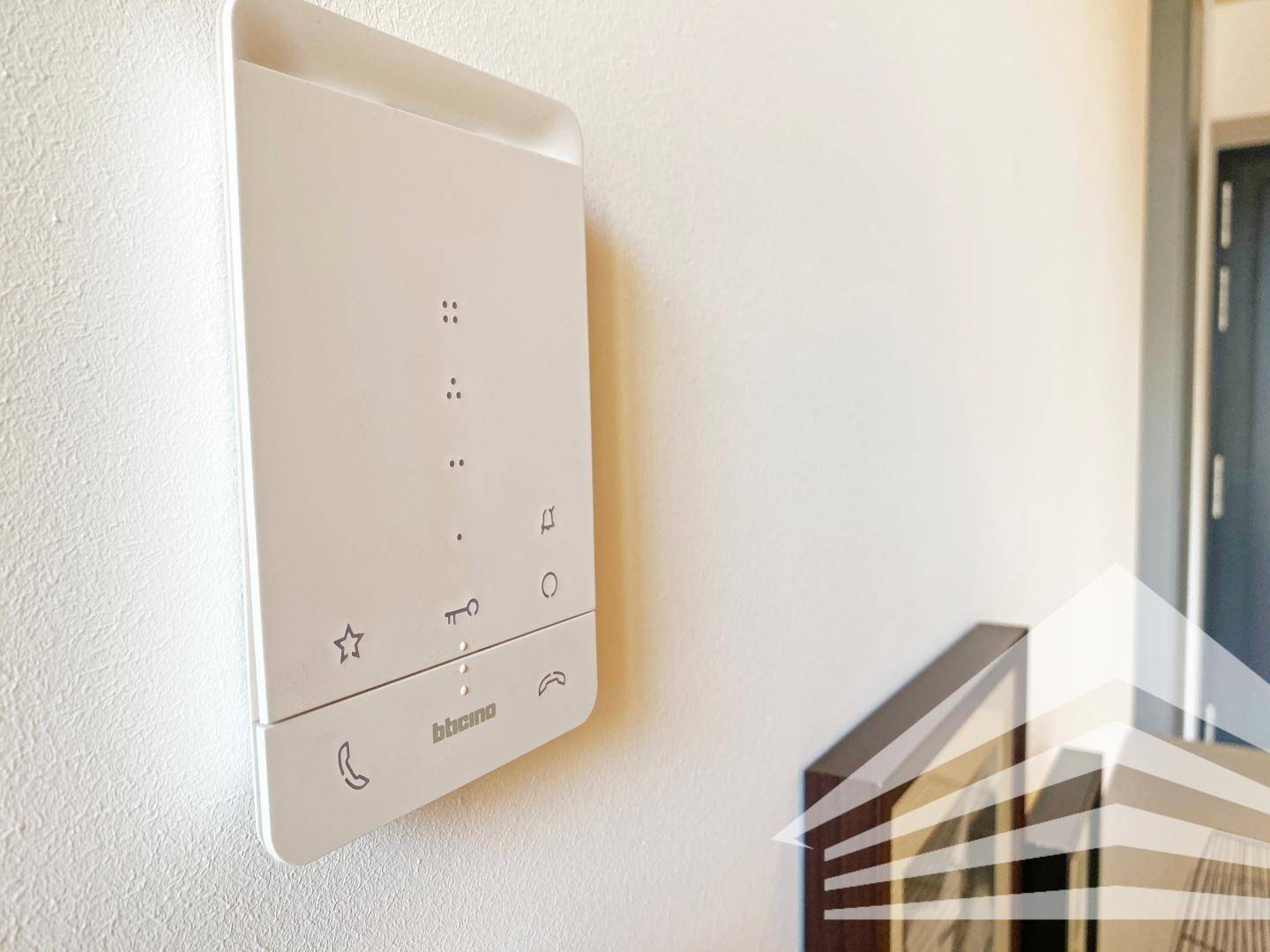 Eine moderne weiße Video-Gegensprechanlage ist an einer hellen Wand im Eingangsbereich montiert.