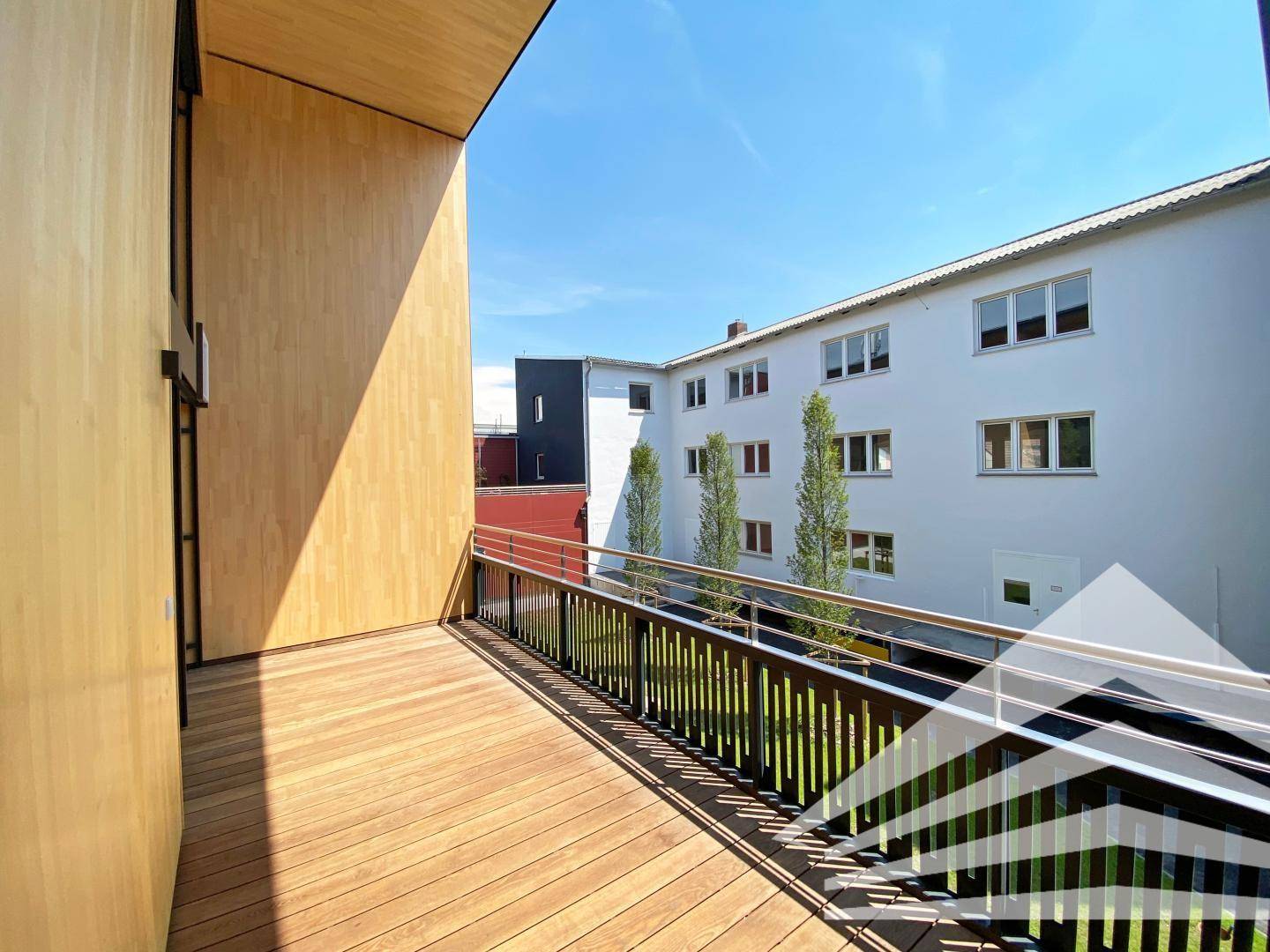 Geräumiger Holzbalkon mit Metallgeländer und Blick auf die umliegenden Gebäude und Bäume.