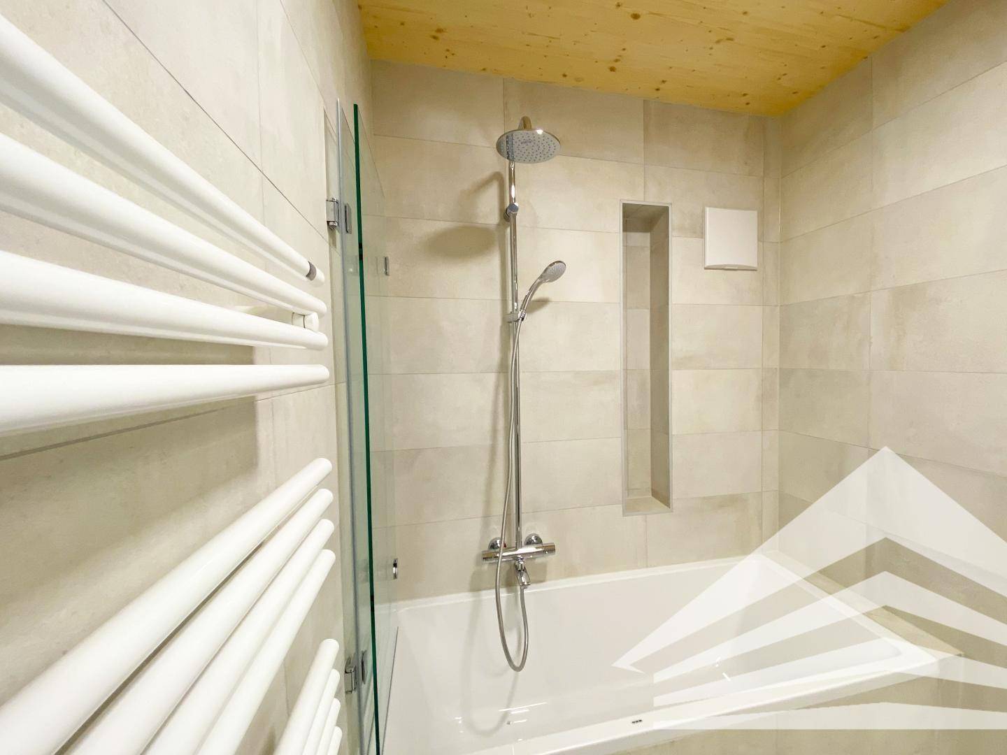 Modernes Badezimmer mit Badewanne, Duscharmatur und beheiztem Handtuchhalter.