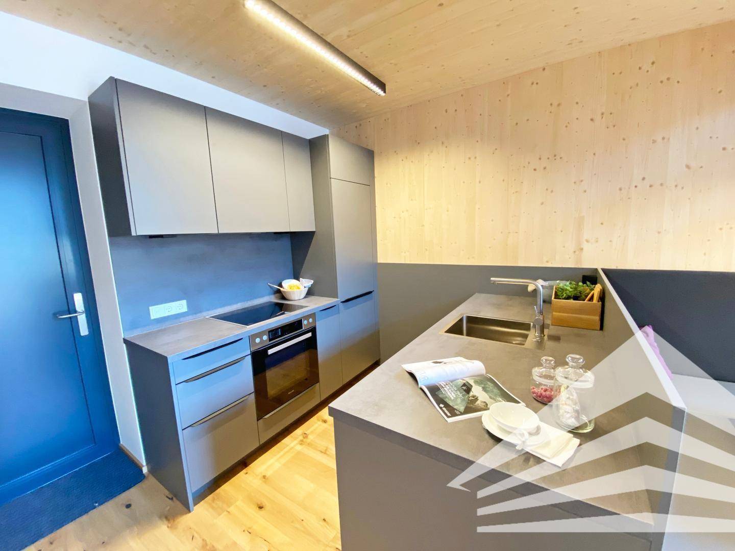 Moderne Küchenzeile mit grauen Schränken, integrierten Geräten und Holzboden.
