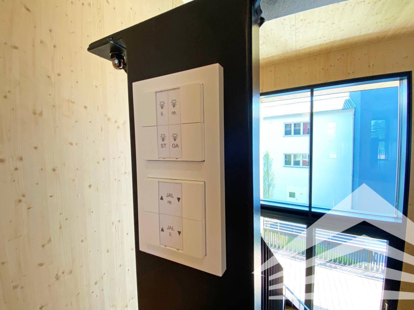 Moderne Lichtschalter an einer dunklen Wand neben einem großen Fenster mit Blick nach draußen.