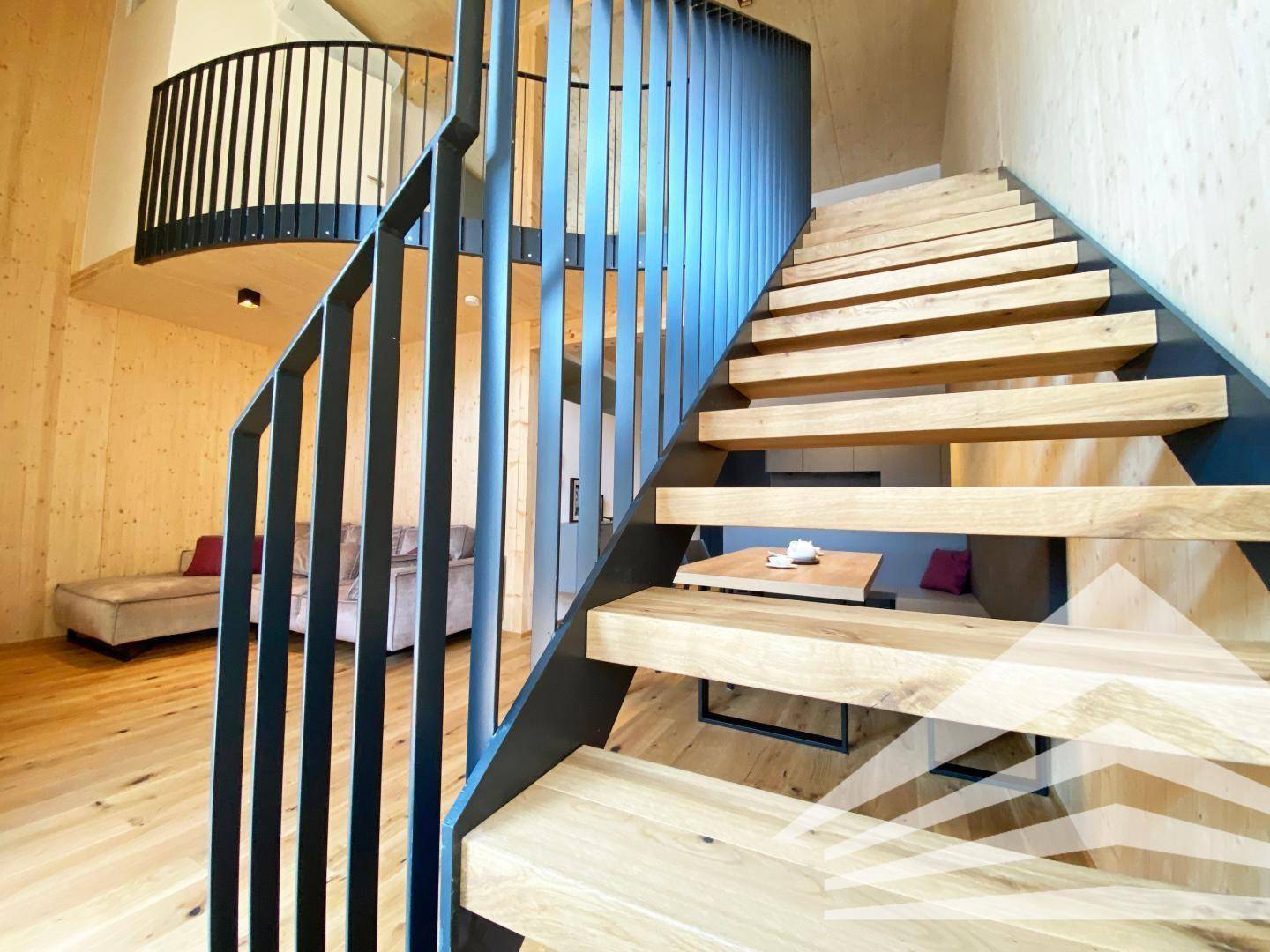 Elegante Holztreppe mit schwarzem Metallgeländer, die zu einer offenen Galerie führt.