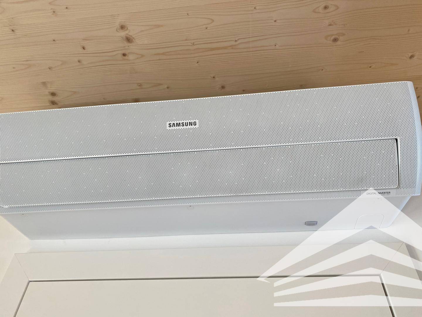 Eine weiße Samsung Klimaanlage ist an einer Holzdecke in einem modernen Raum montiert.