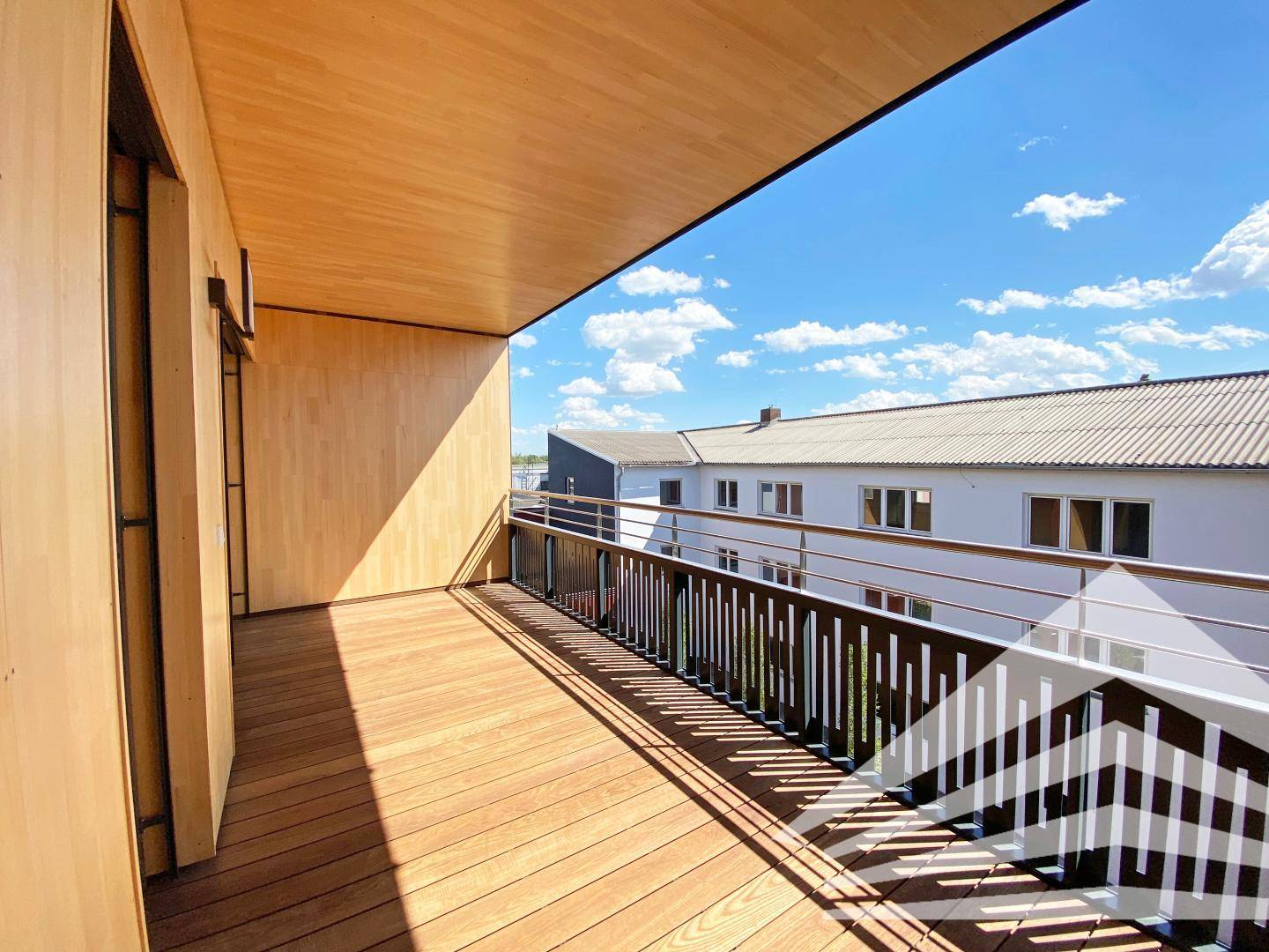 Heller Balkon mit Holzboden und weitem Blick unter blauem Himmel.