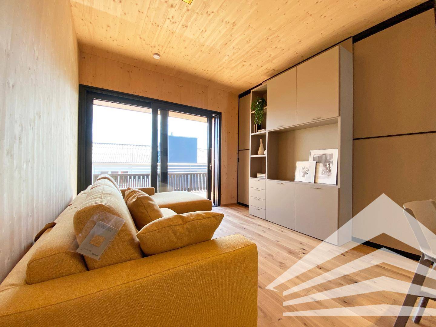 Helles Wohnzimmer mit gelbem Sofa, Einbauschränken und Zugang zu einem Außenbereich.