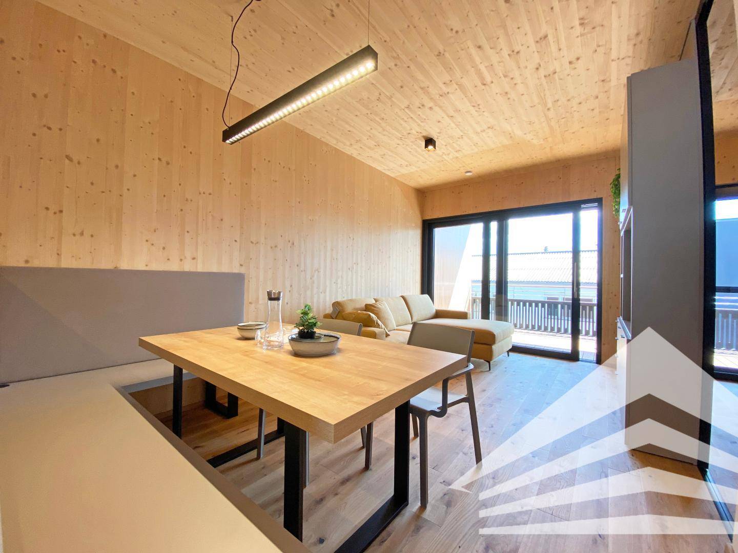 Essbereich mit Holztisch und Sitzbank, angrenzend an den Wohnbereich mit Balkonzugang.