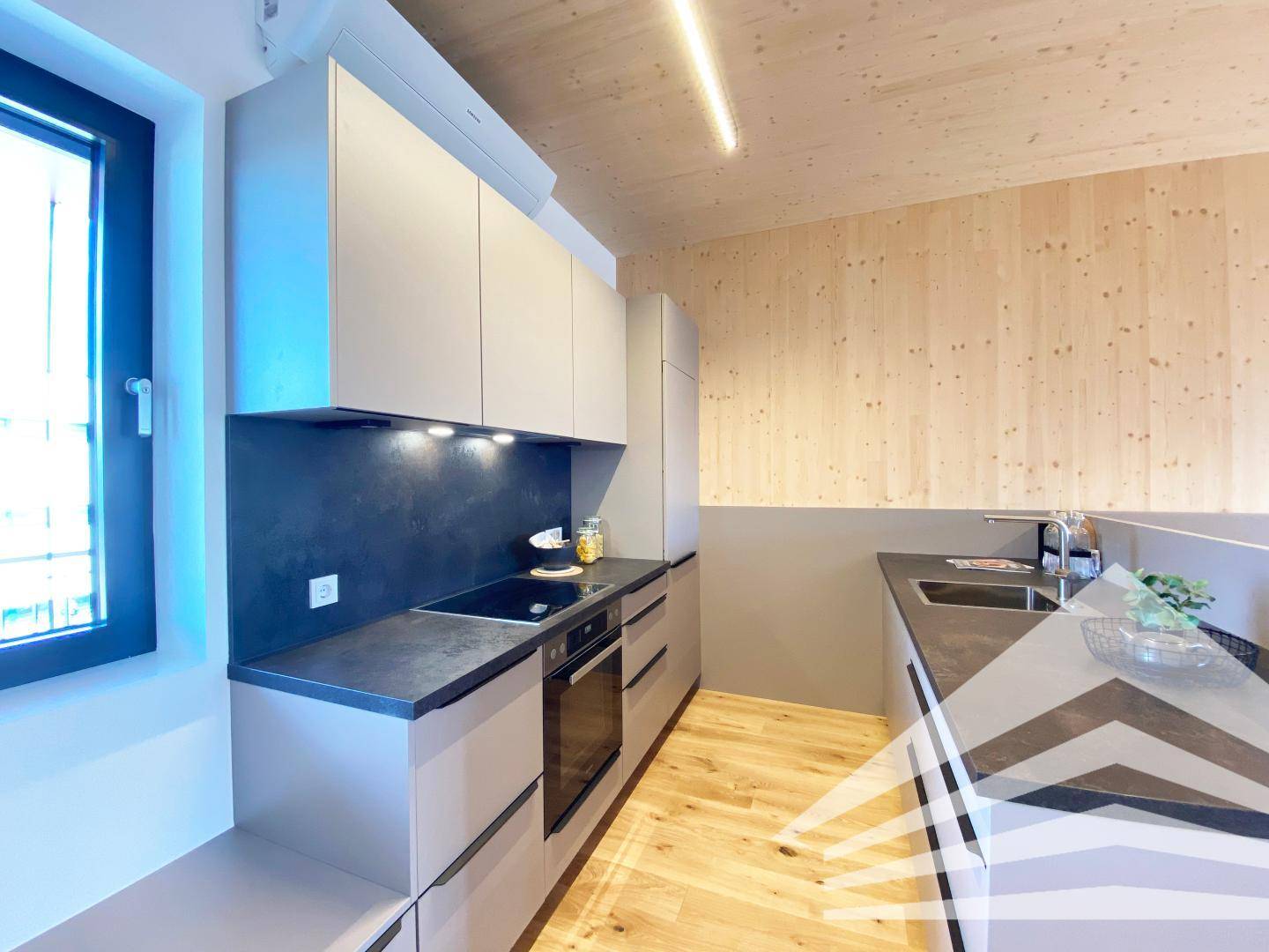 Moderne Küche mit grauen Schränken, dunkler Arbeitsplatte und Induktionskochfeld.