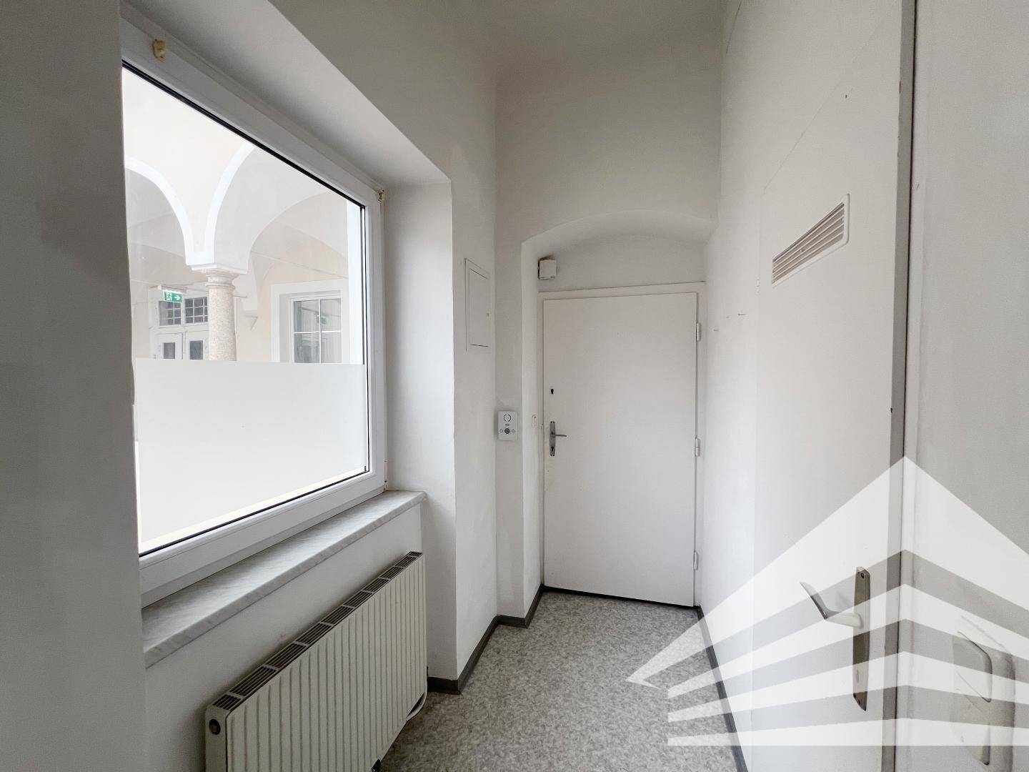 Heller Flur mit Fenster zum Innenhof, Heizkörper und Eingangstür.