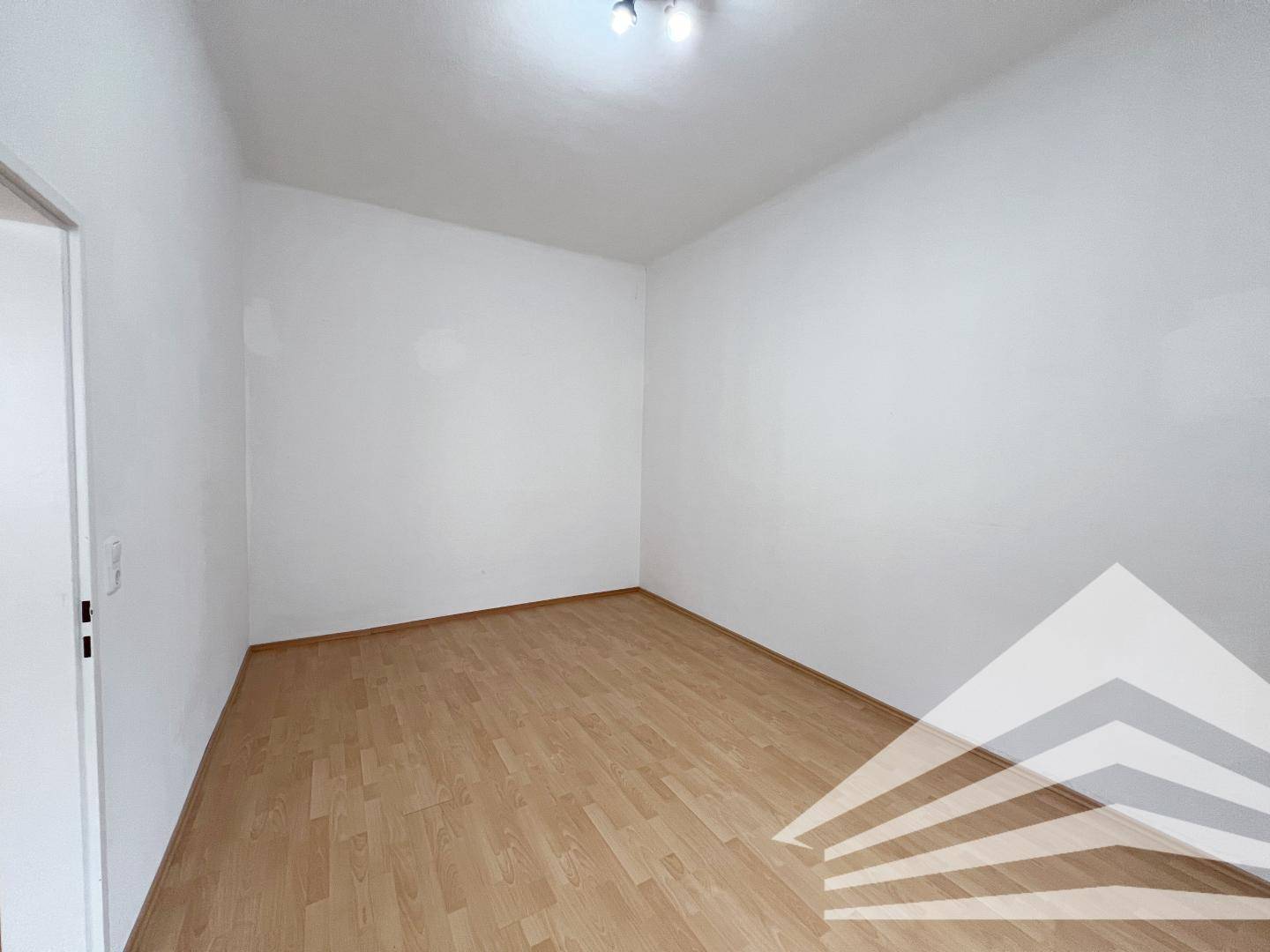 Leeres Zimmer mit hellem Parkettboden und weißen Wänden, bereit zur individuellen Gestaltung.