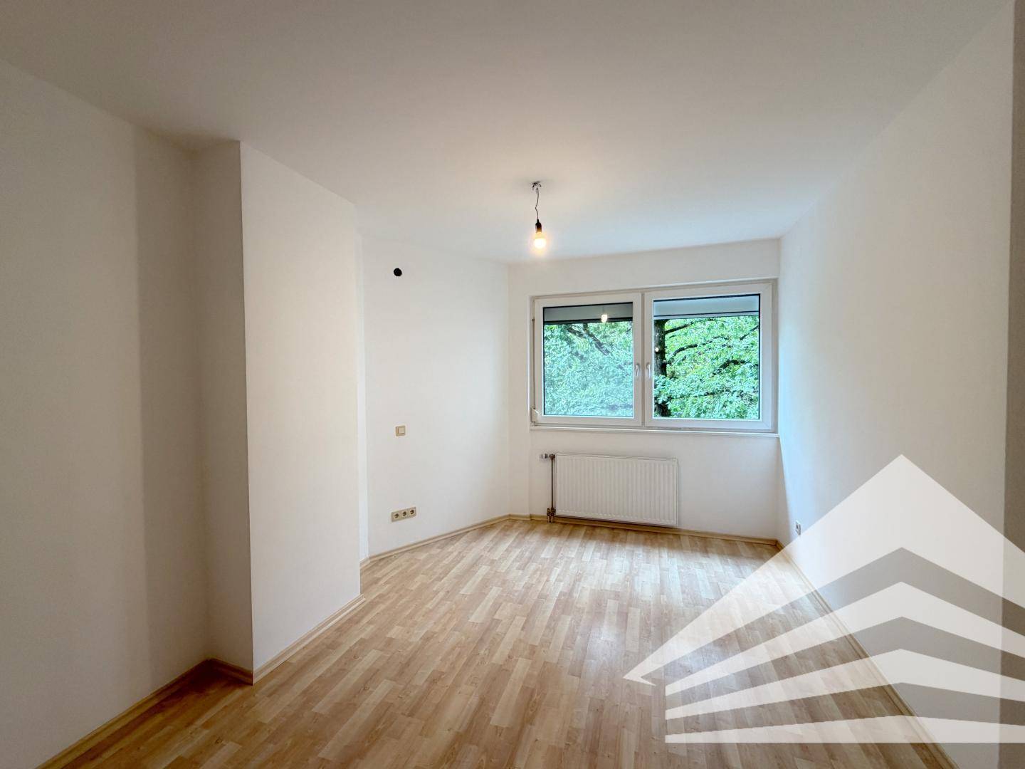 Helles Schlafzimmer mit Laminatboden, weißen Wänden und Fenster mit Blick ins Grüne.