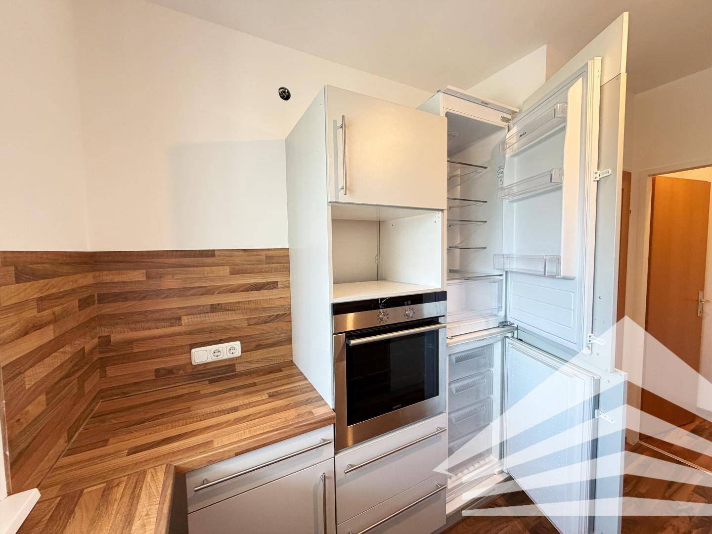 Integrierter Kühlschrank und Backofen in der modernen Küche mit Holzoptik-Elementen.