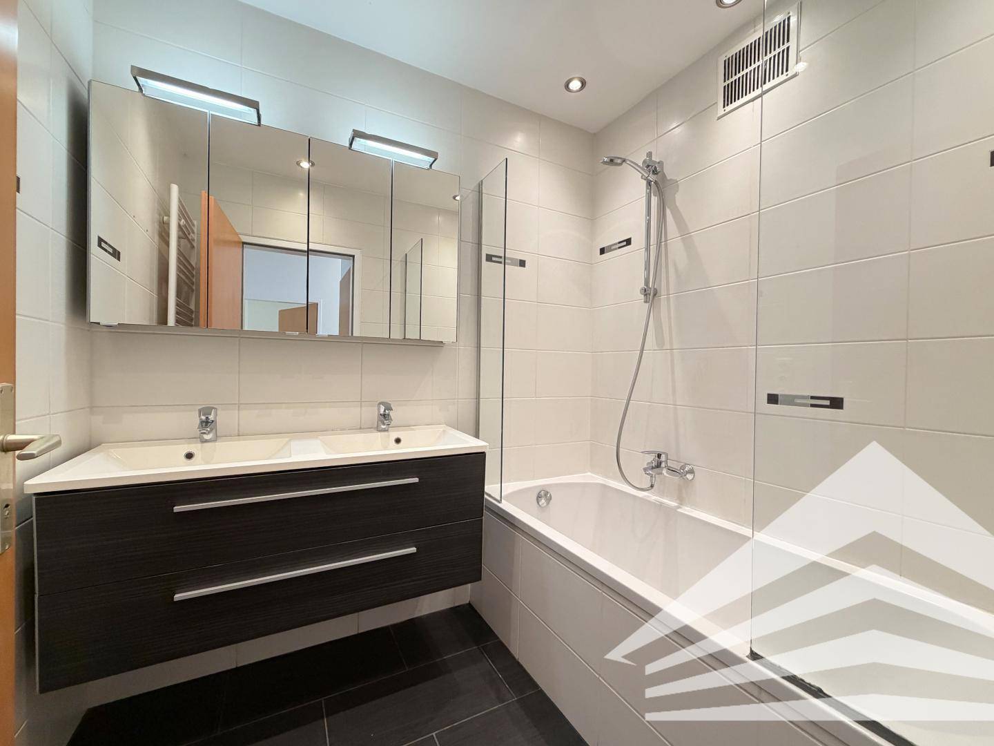 Modernes Badezimmer mit Doppelwaschbecken, Badewanne und weißen Fliesen an den Wänden.