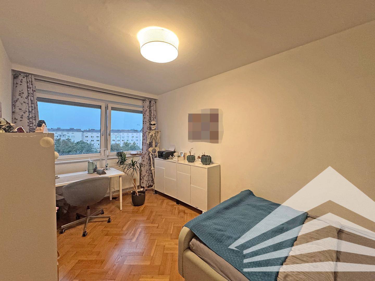 Schlafzimmer mit Parkettboden, Schreibtisch am Fenster und Blick auf die Umgebung.