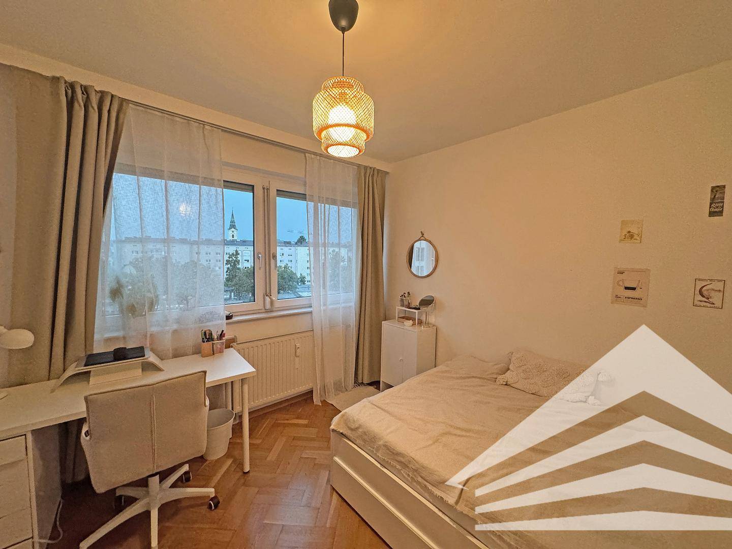 Helles Schlafzimmer mit Parkettboden, Schreibtisch am Fenster und Blick auf die Stadt.