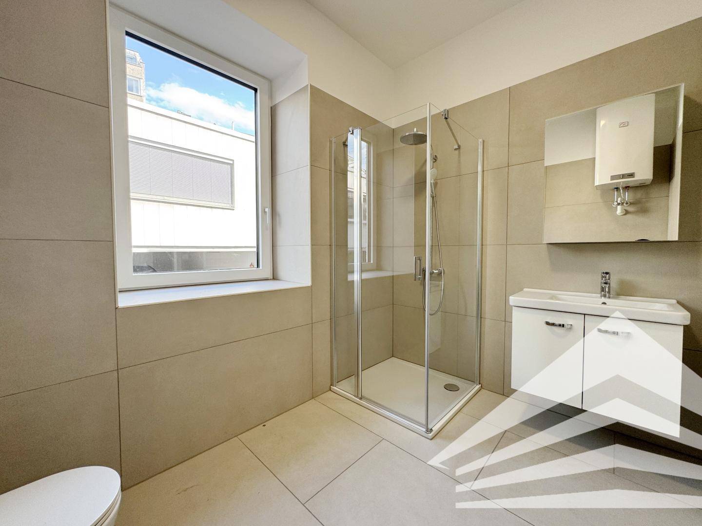Modernes Badezimmer mit beigen Fliesen, Duschkabine und Fenster für Tageslicht.