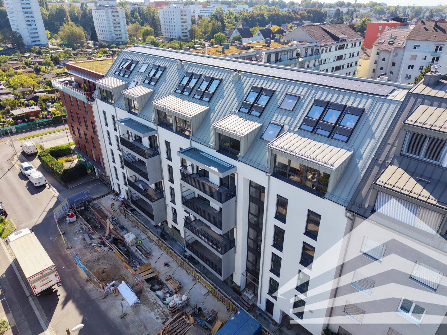 Neubau mit moderner Architektur, Balkonen und Baustelle im Vordergrund unter blauem Himmel.