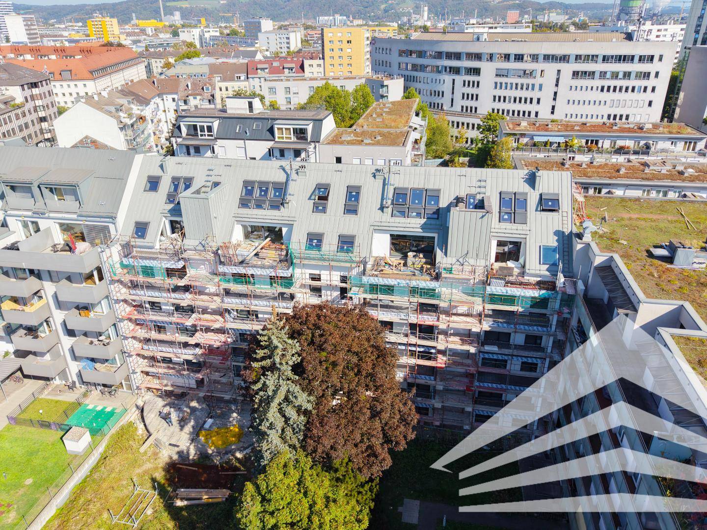 Weitläufige Luftaufnahme eines im Bau befindlichen Wohngebäudes mit Gerüst und Stadtansicht.