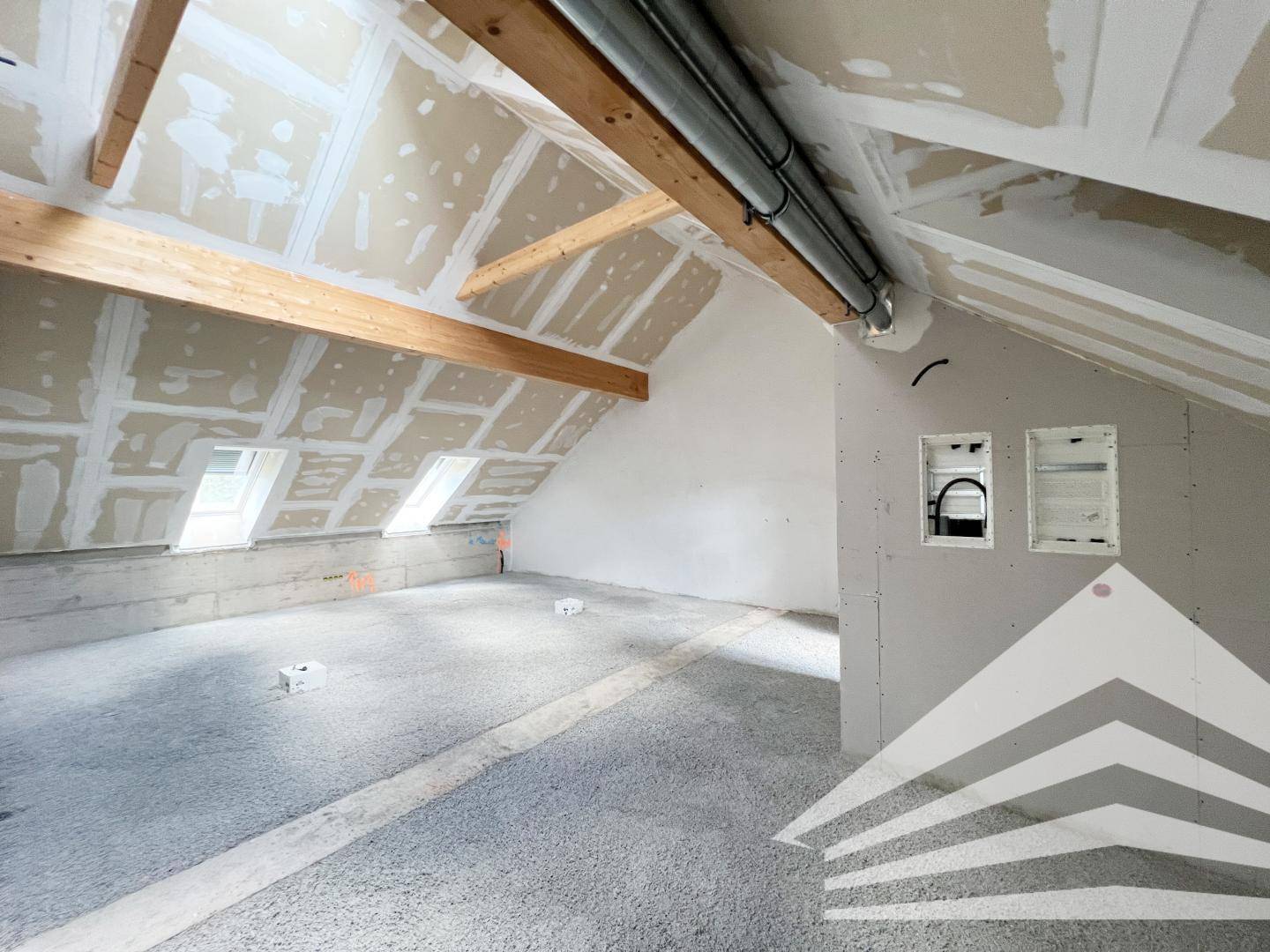 Geräumiger Rohbau mit sichtbaren Holzbalken, schrägen Decken und mehreren Dachfenstern für viel Licht.
