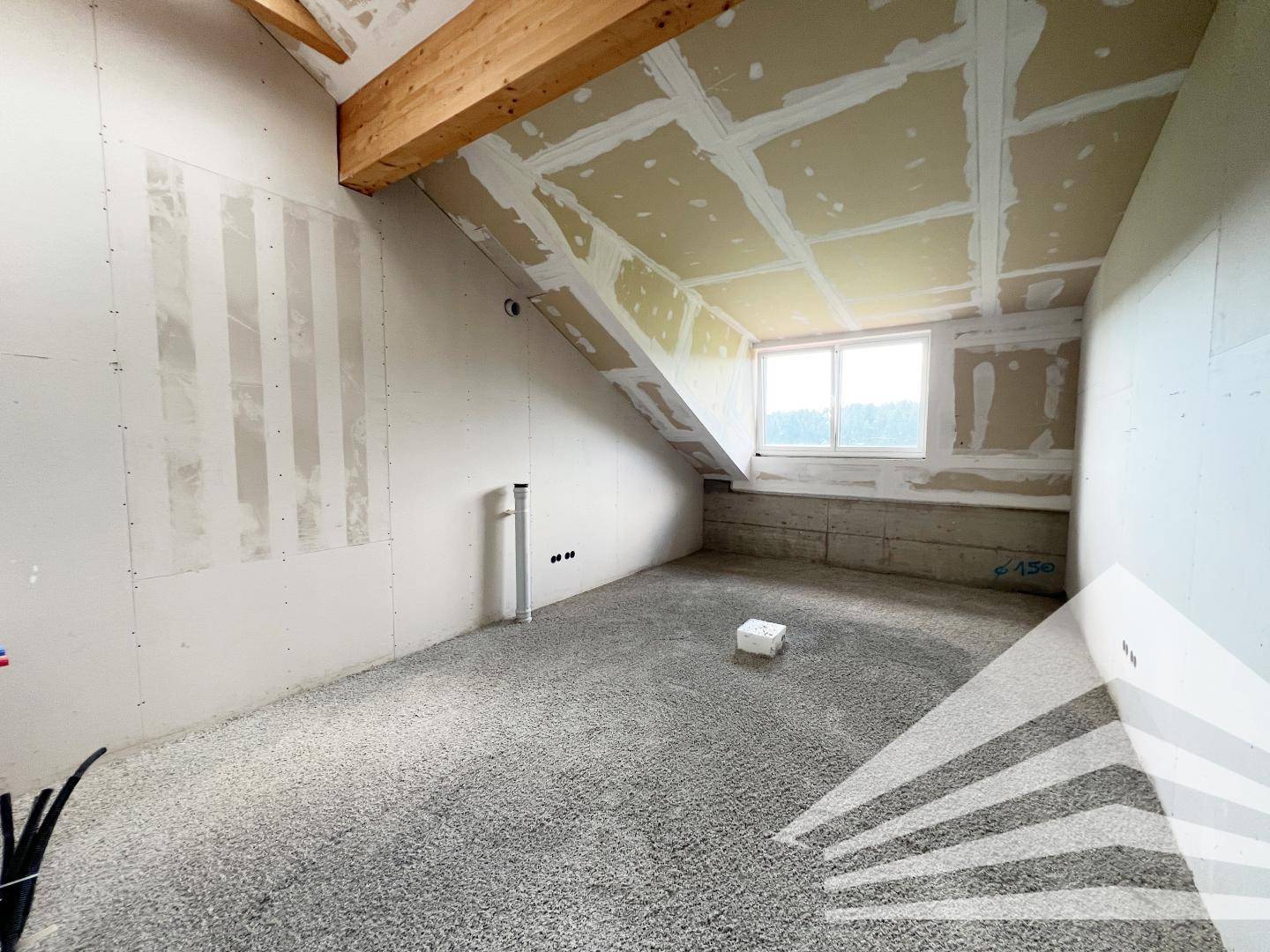 Rohbau eines Raumes mit schrägen Decken, sichtbaren Installationen und Blick auf die Landschaft.