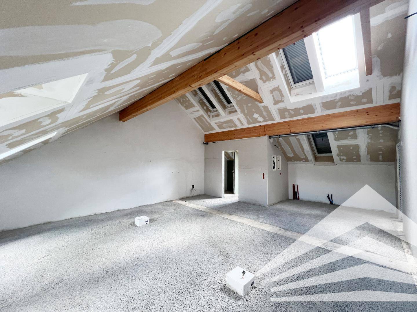 Großer Rohbau mit Holzbalken, schrägen Decken und Dachfenstern, bereit für den Innenausbau.