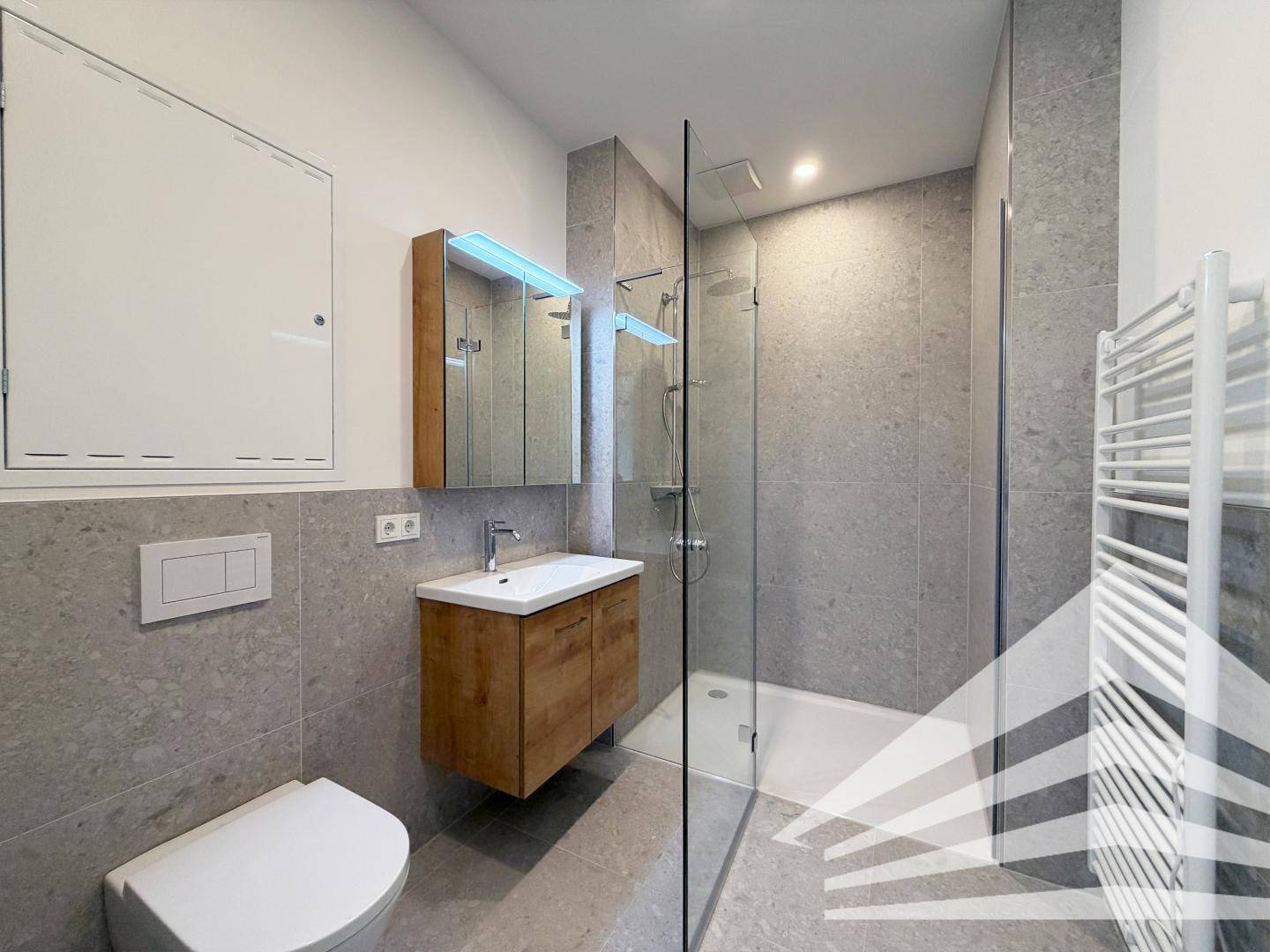 Modernes Badezimmer mit grauen Fliesen, ebenerdiger Dusche und stilvollem Holzwaschtischunterschrank.