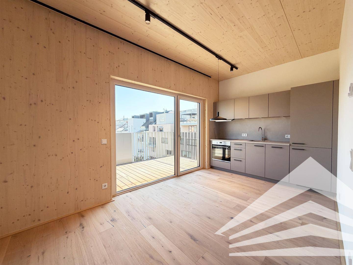 Moderner Wohnbereich mit Holzwänden, integrierter Küche und großem Schiebefenster zum Balkon.