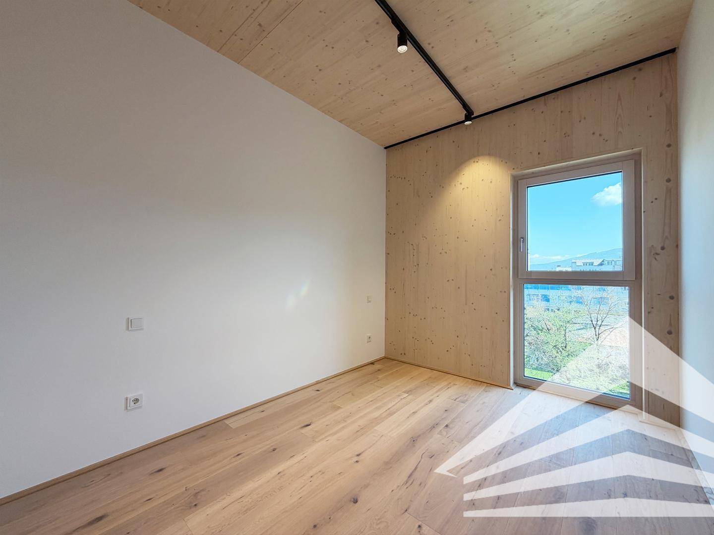 Helles Zimmer mit Holzboden und Holzwand, ideal als Schlaf- oder Arbeitszimmer mit viel Tageslicht.