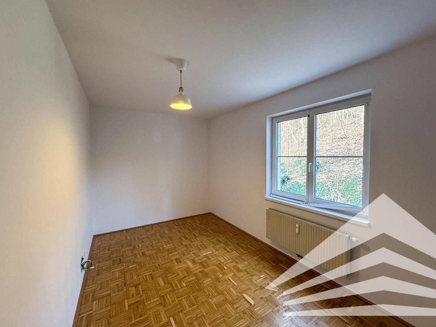 Helles Schlafzimmer mit Parkettboden und Fensterblick ins Grüne, bereit zur individuellen Gestaltung.