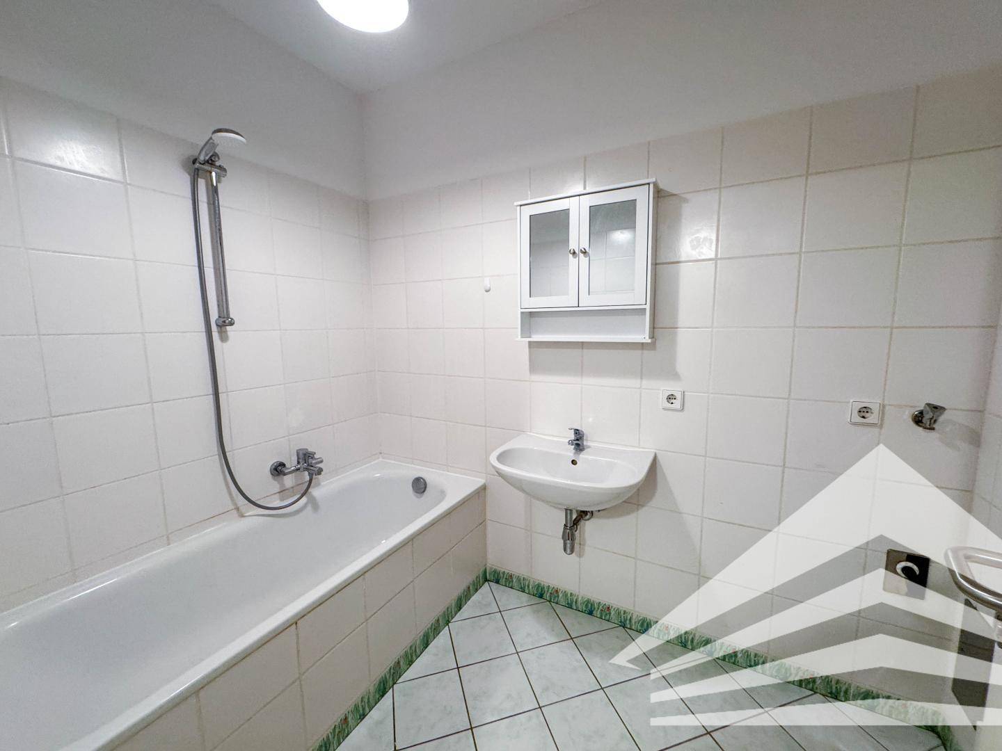 Badezimmer mit Badewanne, Waschbecken und weißen Fliesen, in gutem Zustand.